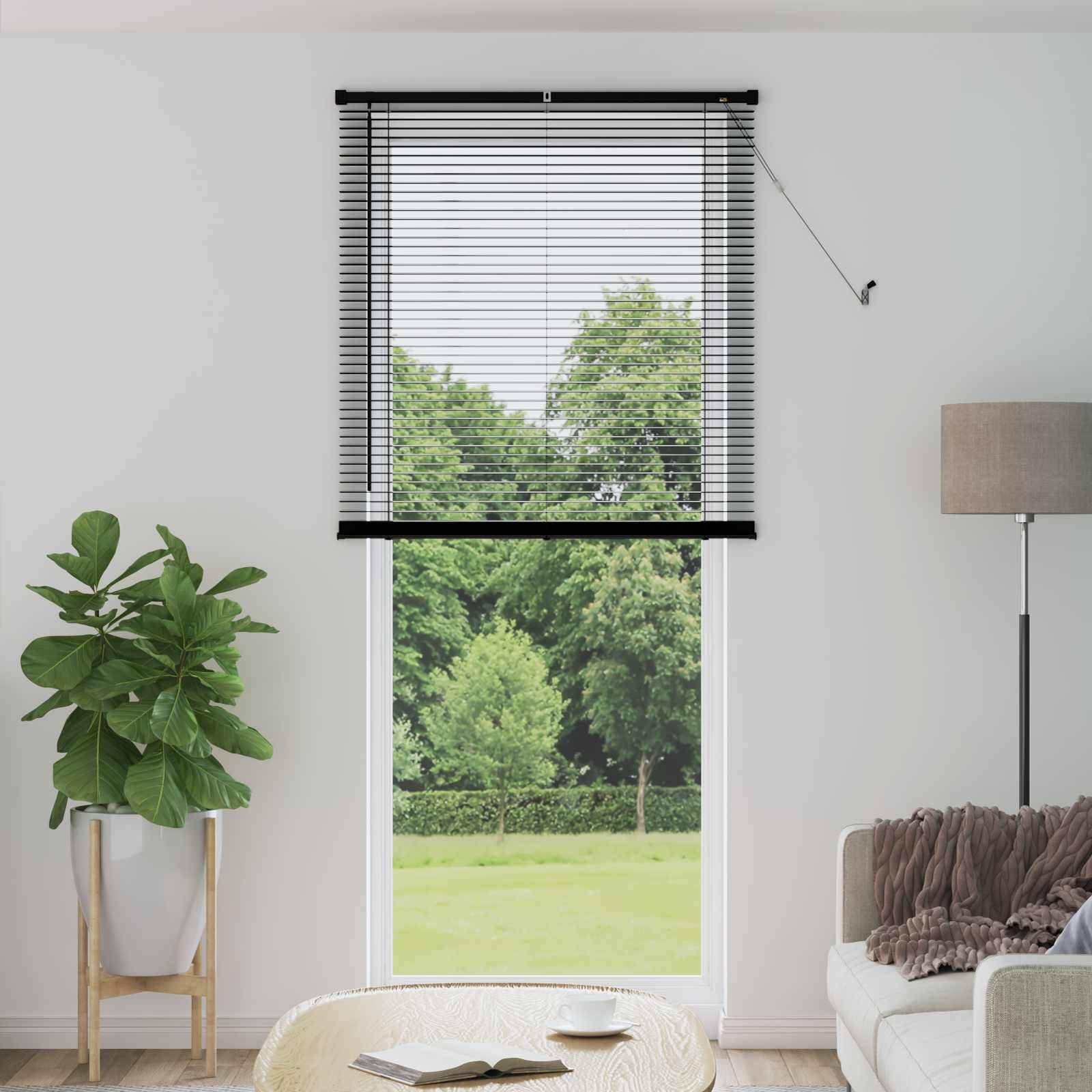 Ein Wohnzimmer mit großem Fensterblick auf grüne Bäume, mit einer Topfpflanze, beigem Sofa, einer Stehlampe und einem Couchtisch.