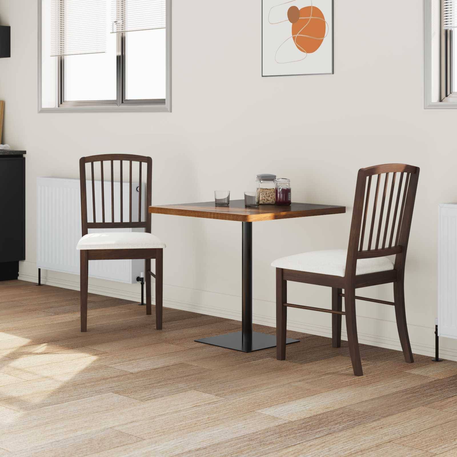 Ein kleiner Essbereich mit einem quadratischen Tisch und zwei Holzstühlen auf einem hellem Holzboden, neben zwei Fenstern mit teilweise geöffneten Jalousien.