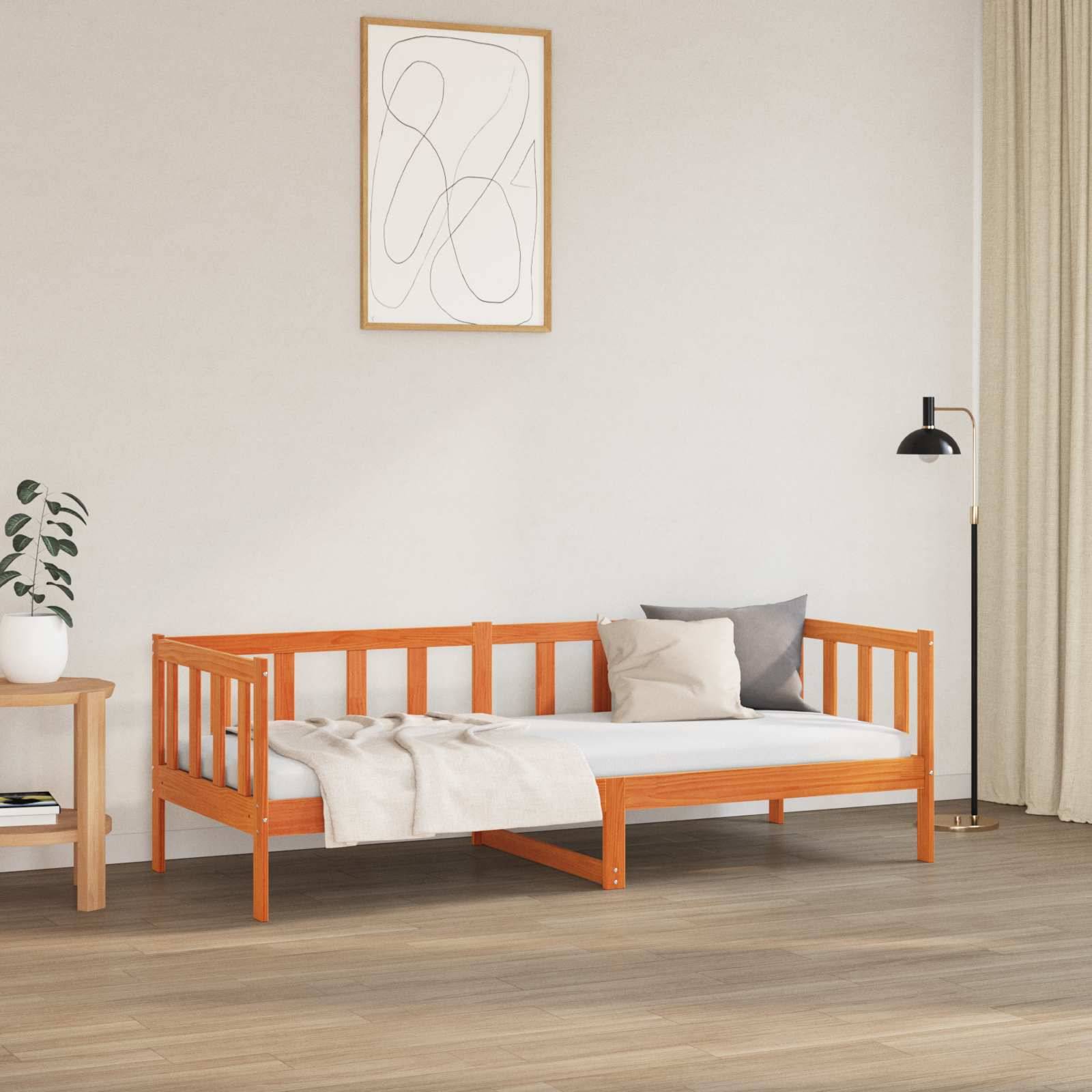 Ein minimalistisches Zimmer mit einem hölzernen Tagesbett, hellgefärbten Kissen, einem kleinen Beistelltisch mit einer Pflanze, Wandkunst und einer Stehlampe neben Vorhängen.