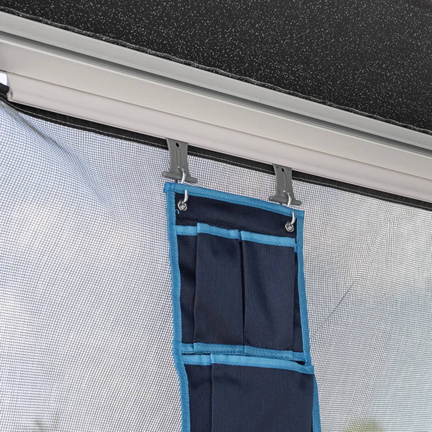 Ein blauer Stoff-Organizer mit Taschen hängt an einer Fliegengittertür und bietet Stauraum für kleine Gegenstände.