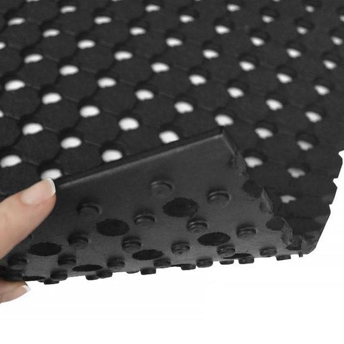 Eine Nahaufnahme einer Hand, die eine schwarze, strukturierte Gummimatte mit sechseckigen Perforationen und erhabenen Noppen hält, die Flexibilität und Griffigkeit zeigt.