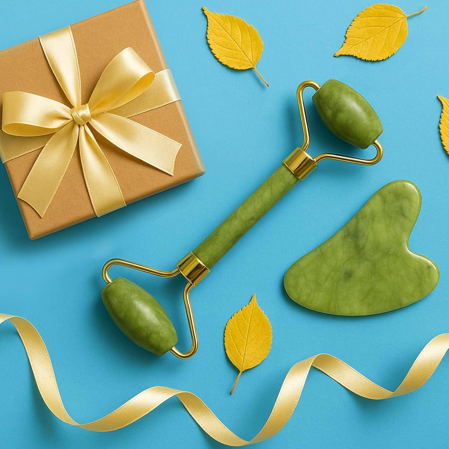 Eine Jade-Rolle und ein Gua-Sha-Werkzeug auf blauem Hintergrund mit verstreuten gelben Blättern und einer eingewickelten Geschenkbox, die mit einem gelben Band gebunden ist.