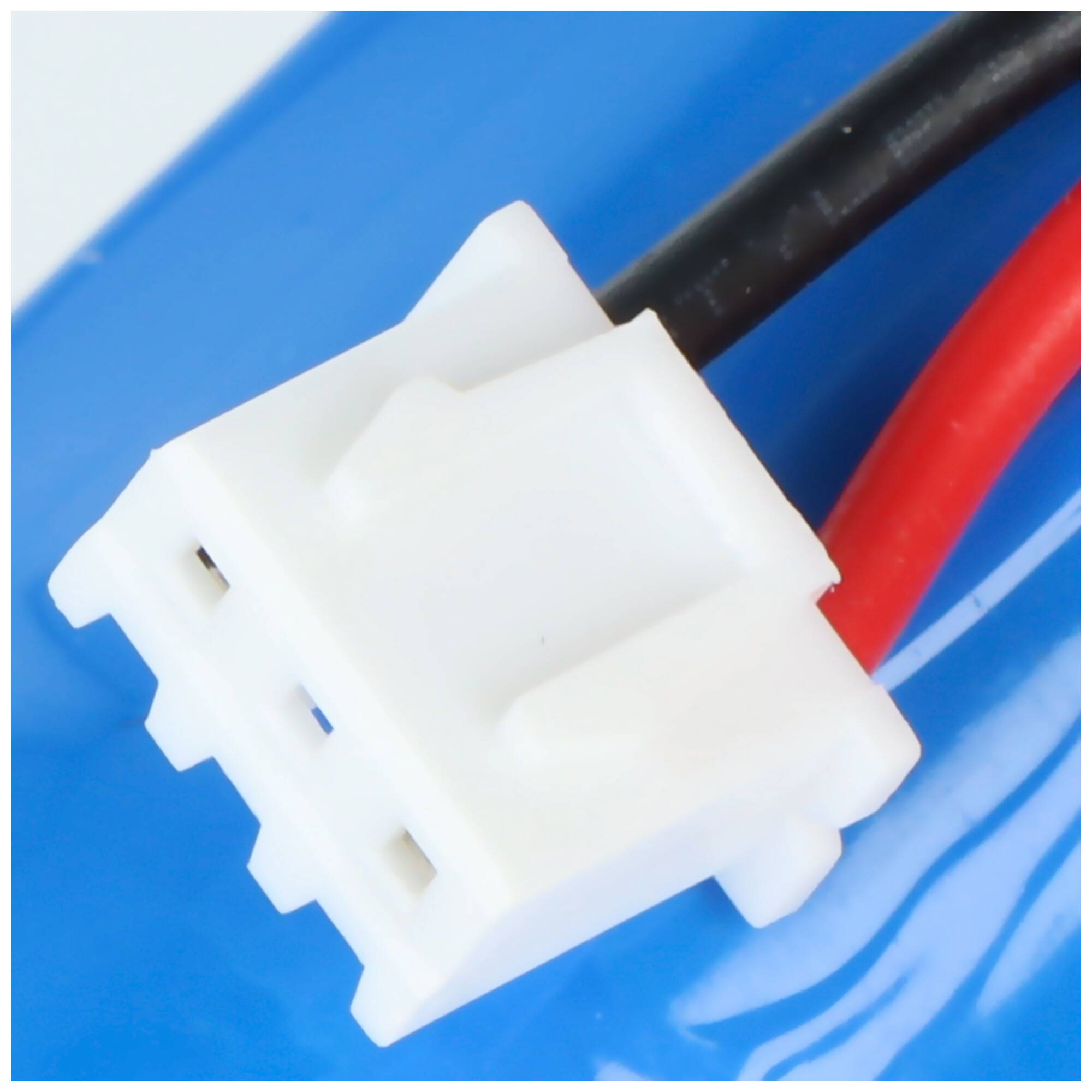 Eine Nahaufnahme eines weißen Elektrosteckers mit drei Stiften, angebracht an roten und schwarzen Drähten vor einem blauen Hintergrund.