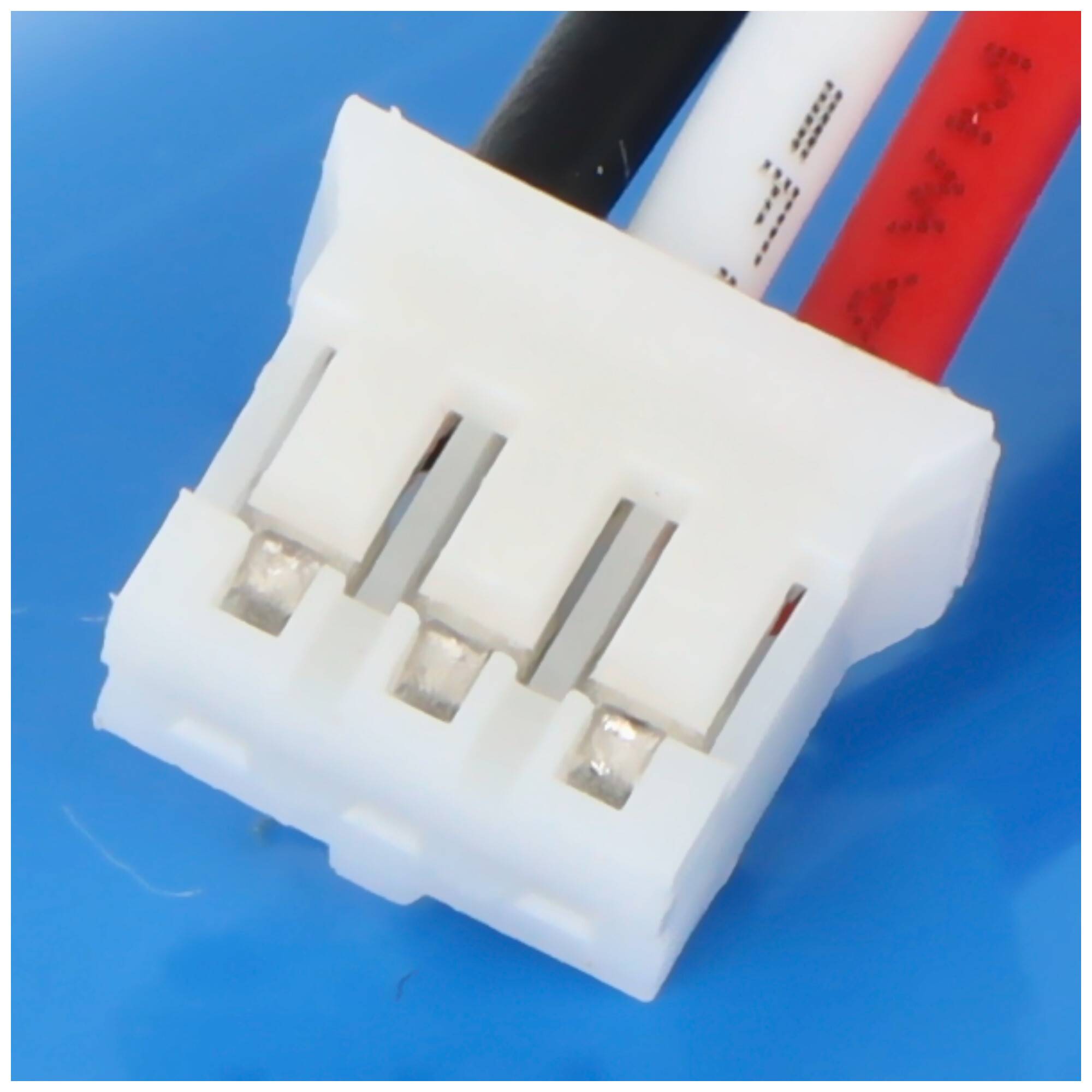 Nahaufnahme eines weißen elektrischen Steckers mit drei Schlitzen und drei Drähten: schwarz, weiß und rot, vor einem blauen Hintergrund.