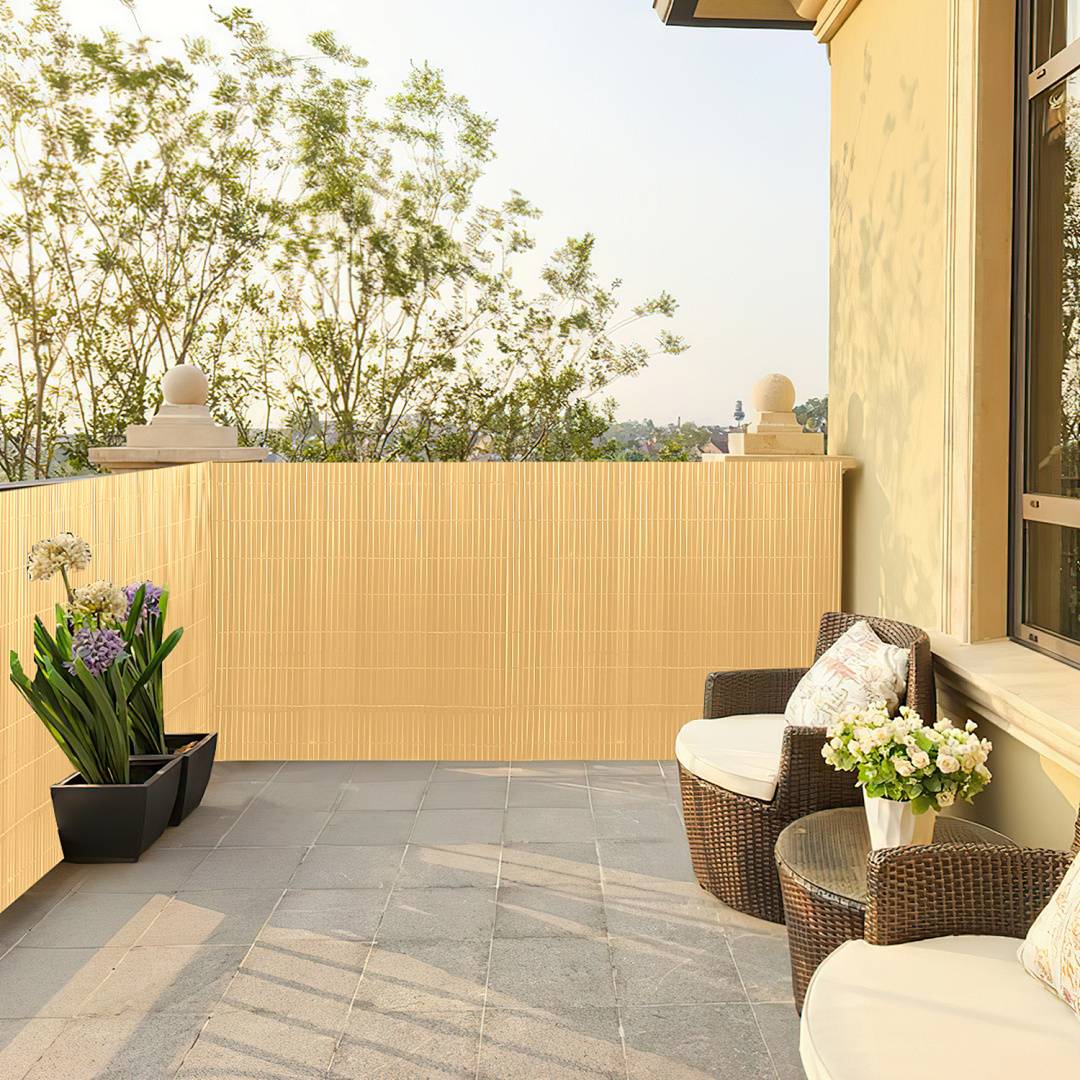 Ein sonniger Balkon mit zwei Korbstühlen und kleinen Tischen, die mit weißen Blumen geschmückt sind, mit Blick auf Bäume und eine malerische Aussicht.
