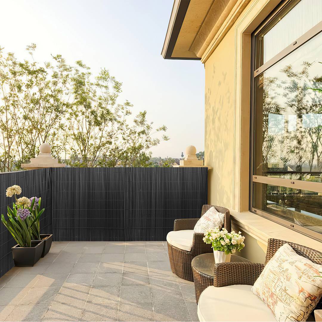 Eine gemütliche Terrasse mit Korbmöbeln und Blumentöpfen mit Blick auf eine grüne Landschaft unter einem klaren Himmel.