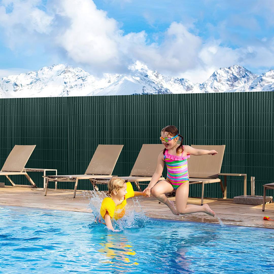 Zwei Kinder spielen an einem Pool mit Bergen im Hintergrund. Ein Kind springt in einem Badeanzug und mit Schwimmbrillen hinein; das andere sitzt in einem aufblasbaren Schwimmgerät.