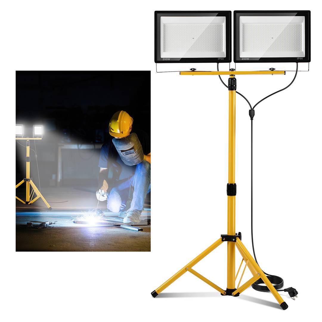 Gelbe LED-Arbeitsleuchte mit Doppelkopf auf Stativ, in Gebrauch durch einen Arbeiter beim Schweißen, beleuchtet den Arbeitsbereich mit hellem Licht.