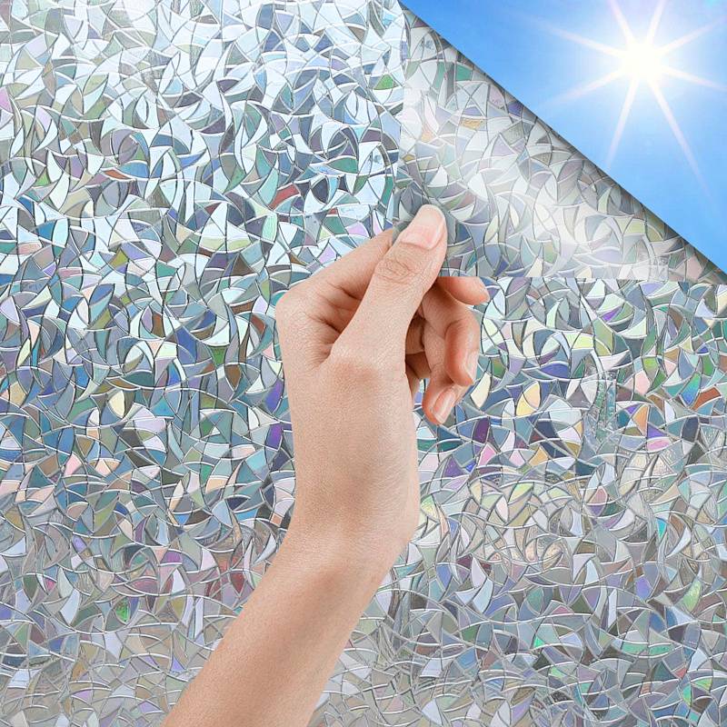 Eine Hand greift auf ein Fenster mit einer prismaartigen Folie zu, die Sonnenlicht reflektiert und mit farbigen Lichtmustern einen Mosaik-Effekt erzeugt.