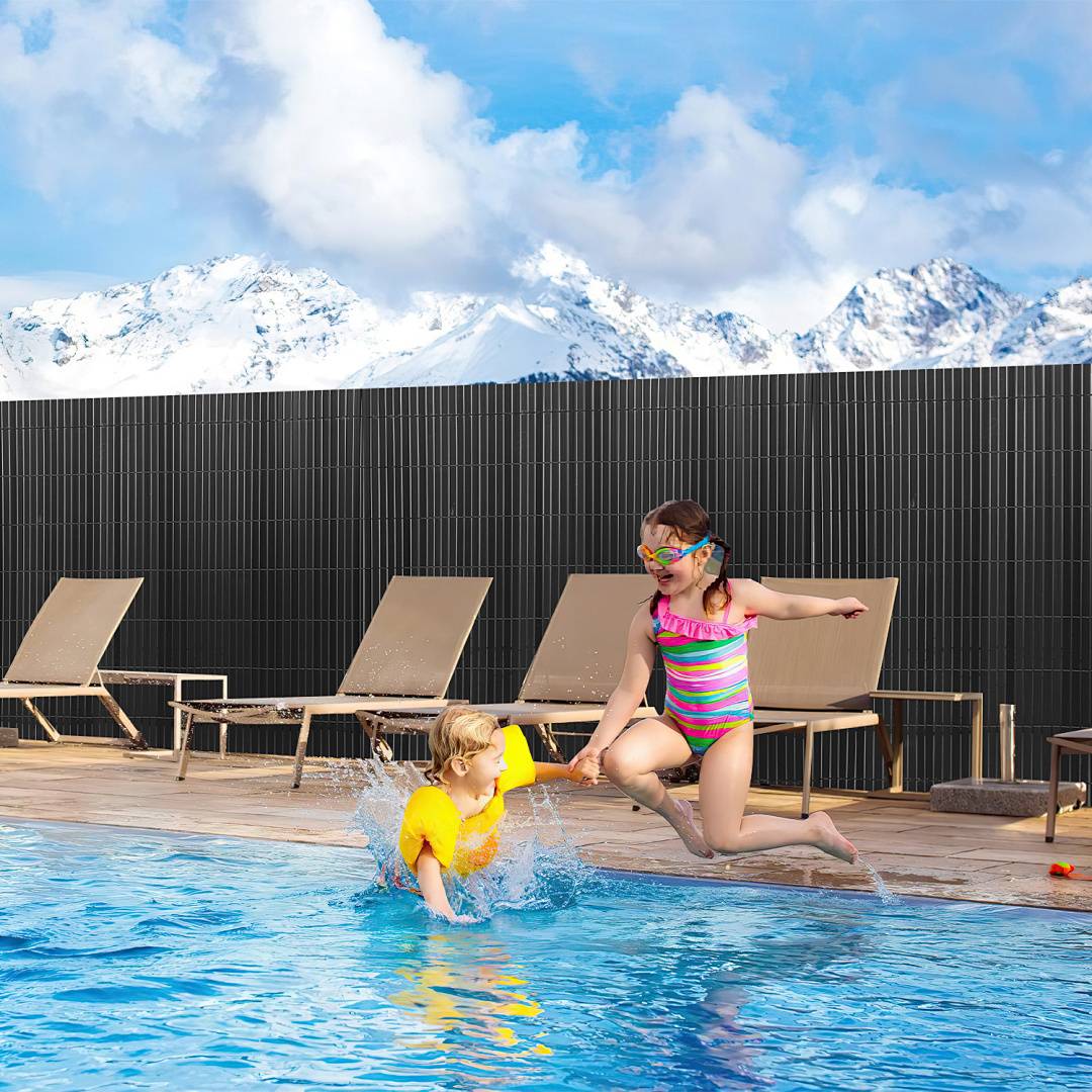 Zwei Kinder in Badeanzügen und Schwimmbrillen spielen neben einem Pool mit verschneiten Bergen und Liegestühlen im Hintergrund.