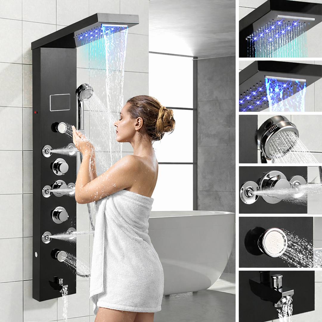 Eine Frau in einem Handtuch stellt ein modernes Duschpanel mit LED-Lichtern und mehreren Düsen neben einer freistehenden Badewanne im gefliesten Badezimmer ein.