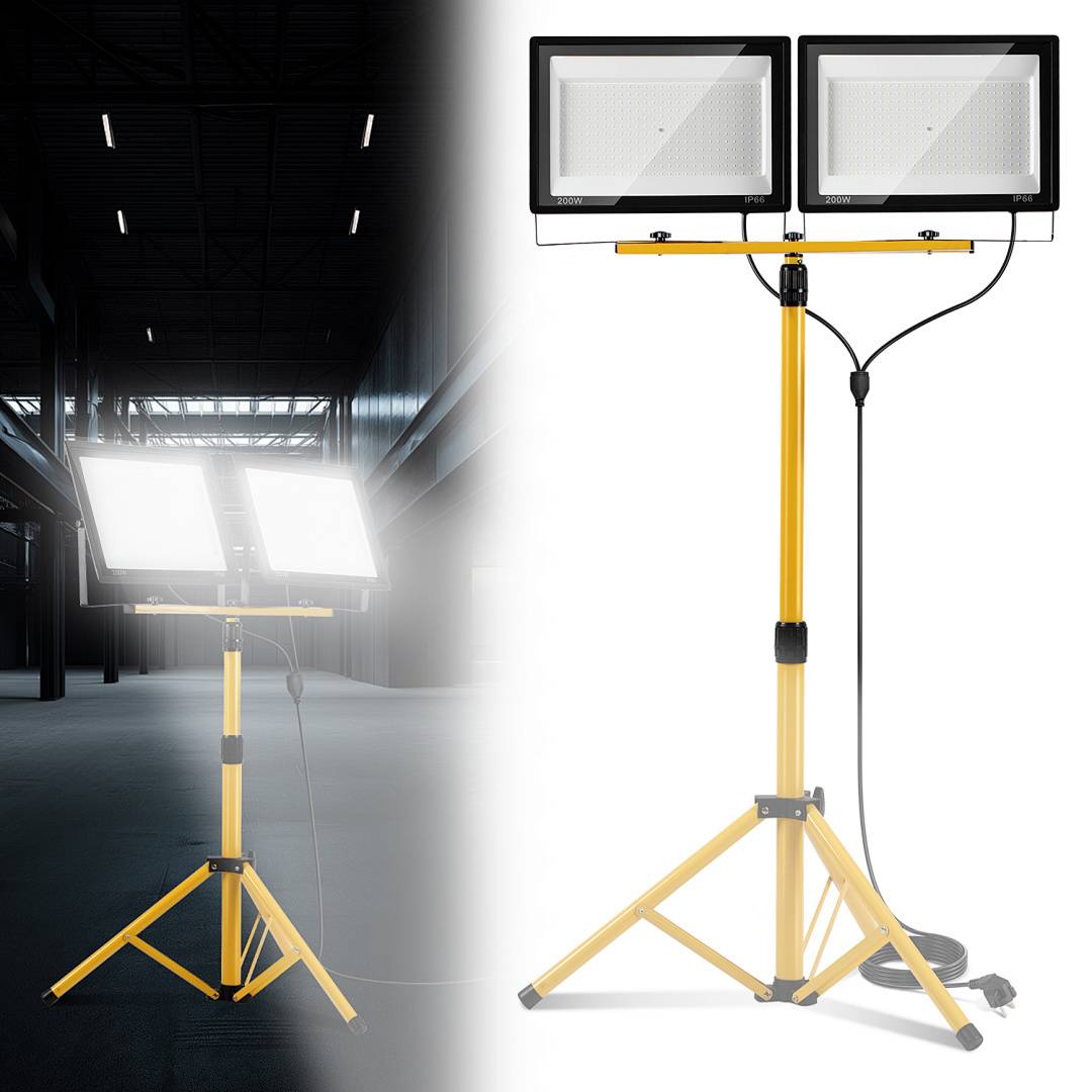Eine LED-Arbeitsleuchte mit Doppelkopf auf einem gelben Stativ, die einen düsteren Industrieraum beleuchtet. Mit verstellbarer Höhe und Schwenkfunktion.