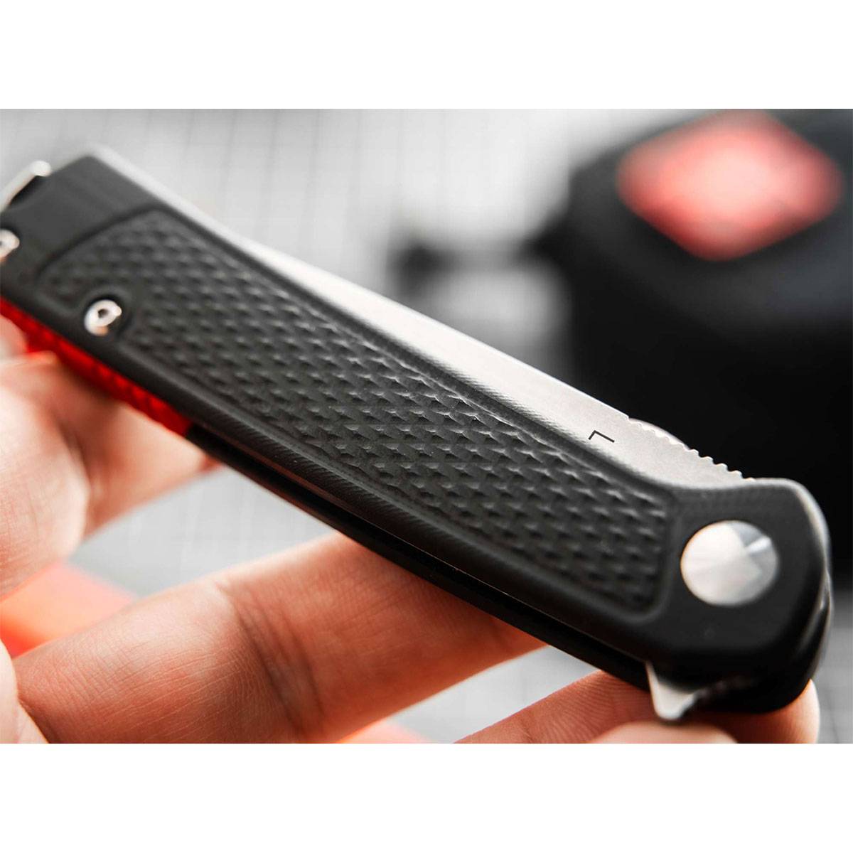 Eine Nahaufnahme eines schwarz-griff igen Falt-Universalmessers, das gehalten wird, zeigt seine strukturierte Griffoberfläche und einen Teil der Klinge, unscharfer Hintergrund.