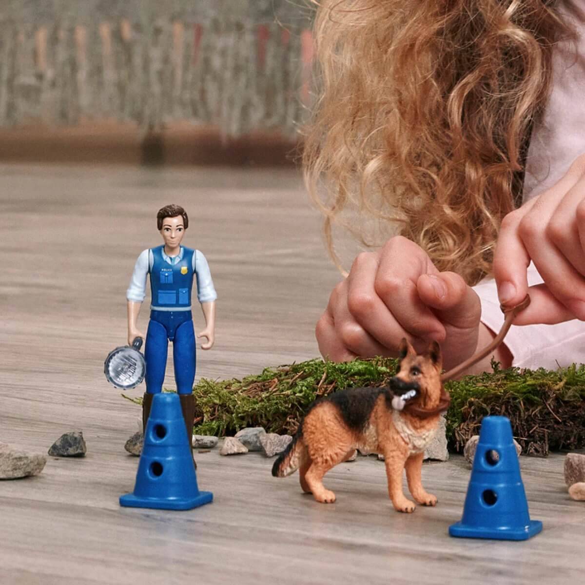 Ein Kind spielt mit Spielfiguren auf einem Holzboden; enthält einen Bauarbeiter und einen Hund, umgeben von kleinen Steinen und Moos.