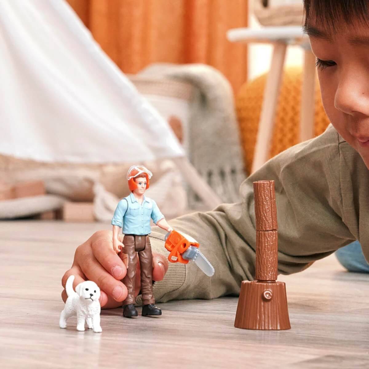 Ein Kind spielt mit einer Bauarbeiter-Spielzeugfigur, komplett mit Helm und Kettensäge, neben einer kleinen weißen Hundefigur im Innenbereich.