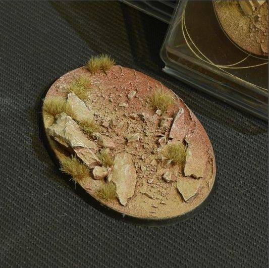 Eine strukturierte Basis mit felsigem Gelände und Grasbüscheln, die eine miniaturhafte Wüstenlandschaft ähnelt.