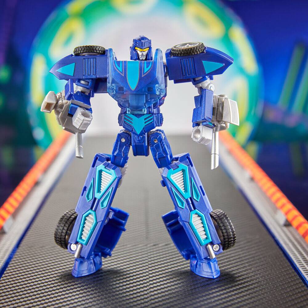Ein blau-silberner Roboterspielzeug steht auf einem futuristischen Gehweg, hält zwei Waffen in den Händen, mit einem unscharfen, farbenfrohen Hintergrund, der Aktion oder Bewegung andeutet.