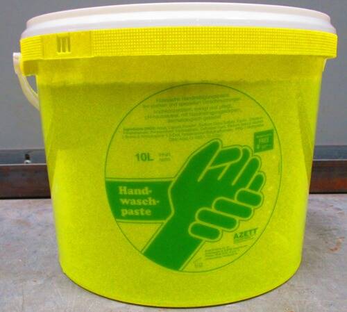 Ein gelber Behälter mit einem grünen Etikett, das ein Bild von zwei Händen beim Waschen zeigt. Der Text lautet „Handwaschpaste