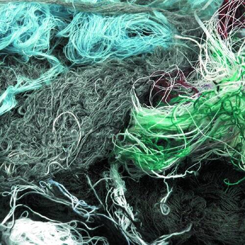 Nahaufnahme einer verworrenen Garnmasse in Grün-, Blau- und Grautönen, die die Textur und Komplexität verflochtener Fasern zeigt.