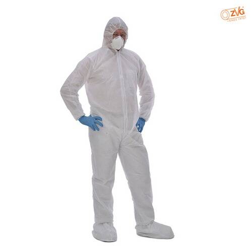 Eine Person in einem weißen Schutzanzug, Handschuhen und Maske, stehend vor einem einfachen Hintergrund, zeigt Schutzausrüstung.