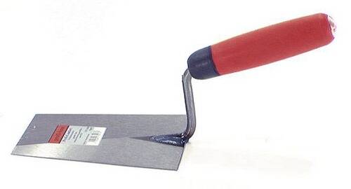 Eine Nahaufnahme einer Maurerkelle mit rotem Griff, die Mörtel auf einer Oberfläche verteilt, was eine Bau- oder DIY-Aufgabe veranschaulicht.