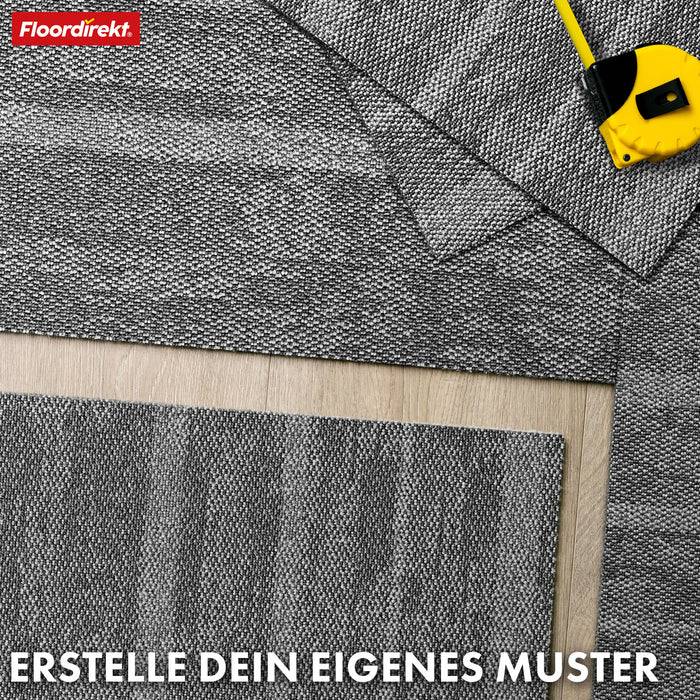 Eine strukturierte graue Teppichfliese überlappt teilweise einen hellen Holzboden. Ein gelbes Stahllineal liegt in der Nähe. Der Text lautet: „Erstelle dein eigenes Muster