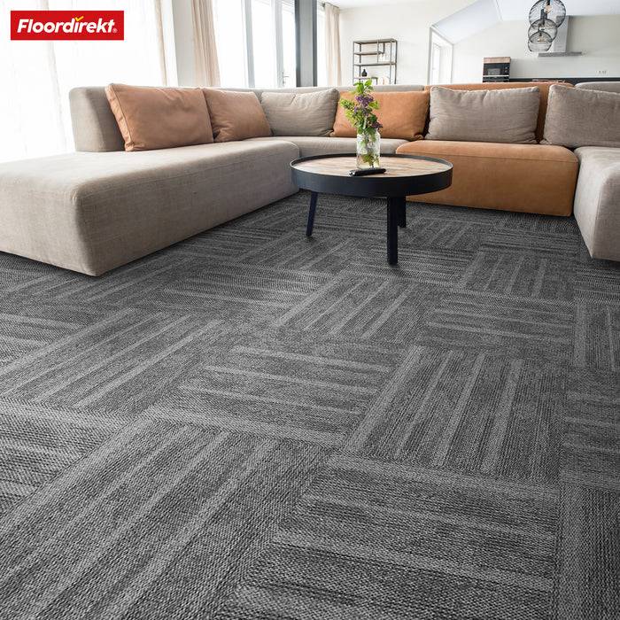 Ein modernes Wohnzimmer mit einem großen L-förmigen Sofa in neutralen Tönen, einem runden Couchtisch mit Pflanzen und gemusterten grauen Teppichfliesen.