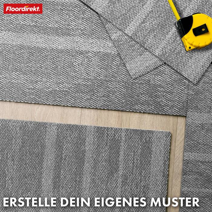 Eine Vielzahl von grauen Teppichfliesen, die auf einem Holzboden angeordnet sind, mit einem Stahllineal. Der Text lautet „ERSTELLE DEIN EIGENES MUSTER.