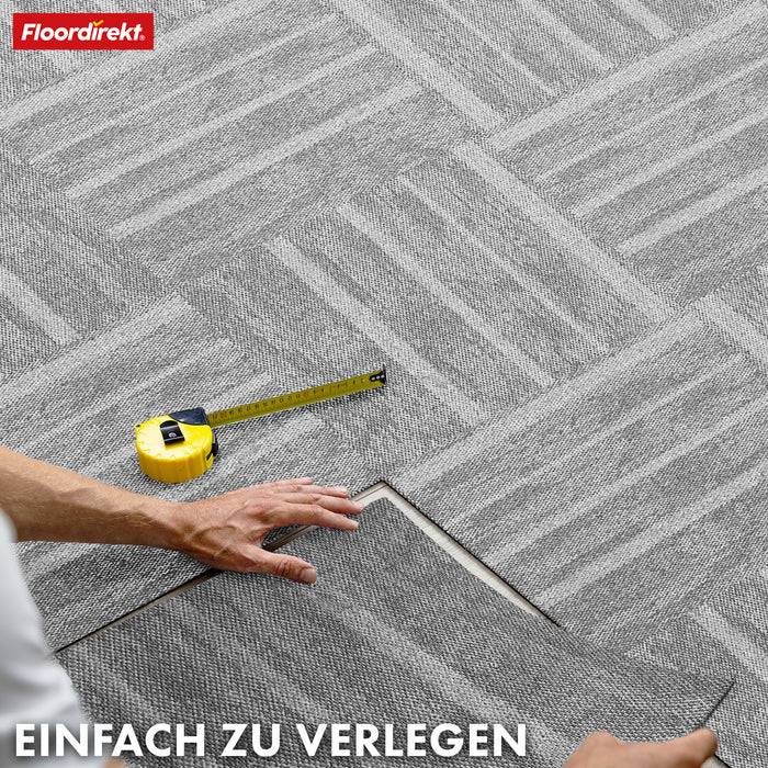 Ein Person verlegt ineinander greifende graue Teppichfliesen mit einem Messstab in der Nähe. Der Text oben links lautet „Floordirekt
