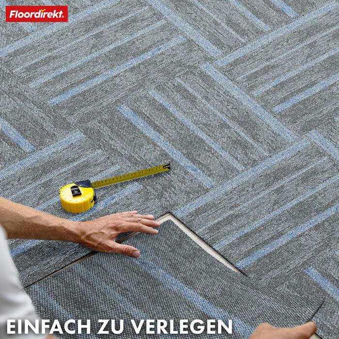 Person, die graue und blaue verzahnte Teppichfliesen mit einem gelben Maßstab in der Nähe anordnet. Der Text lautet „Einfach zu verlegen