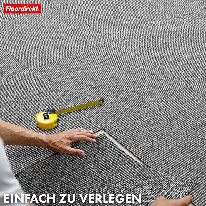 Eine Hand verlegt graue Teppichfliesen mit sichtbarem gelbem Messstab. Der Text lautet „Einfach zu verlegen