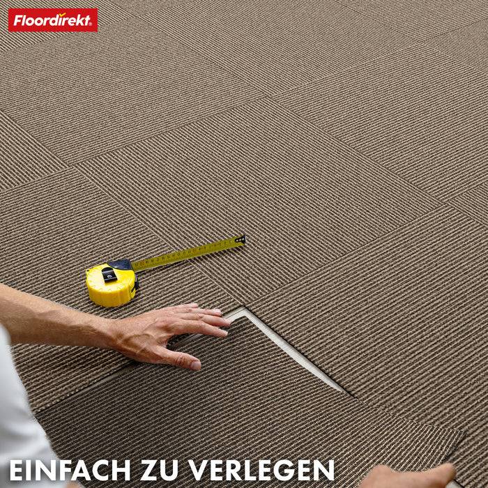 Eine Hand stellt braune Teppichfliesen neben ein Maßstab ein. Logo oben links: Floordirekt. Text unten: Einfach zu verlegen.