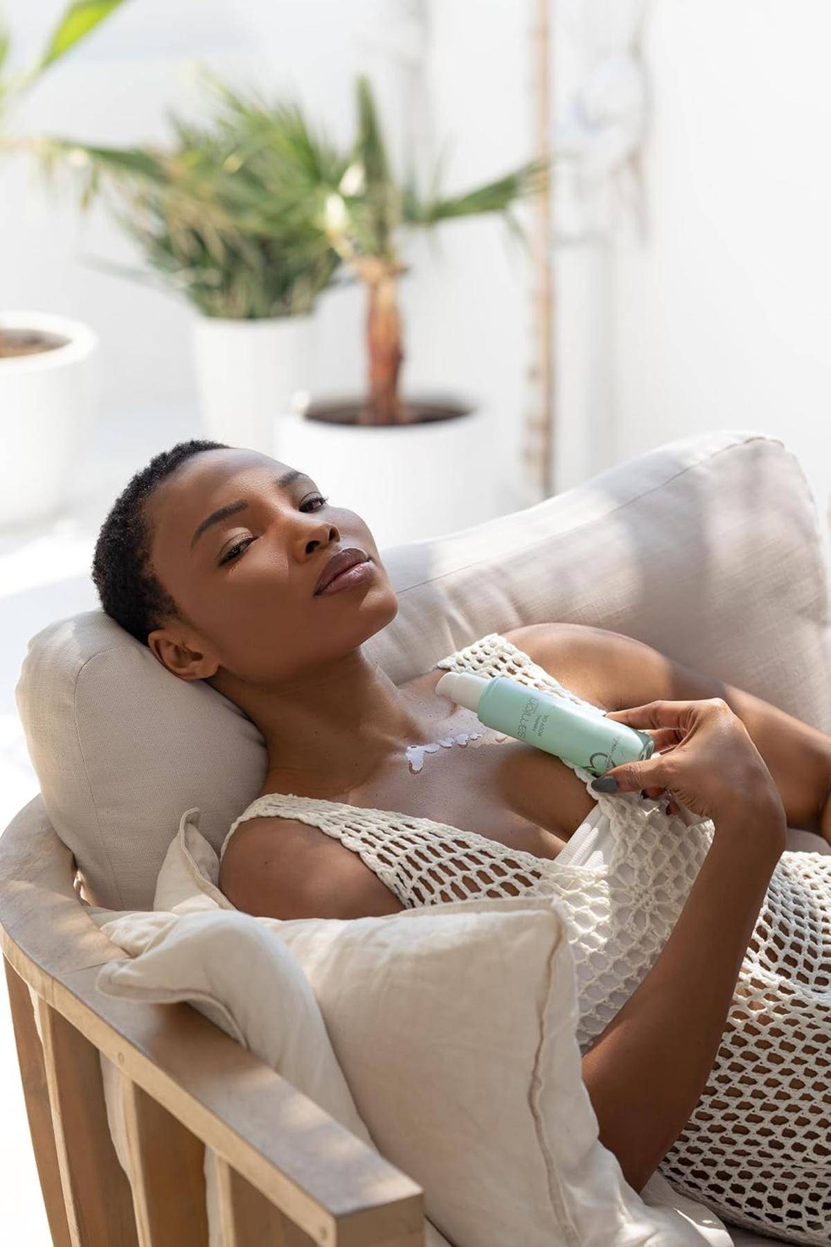 Eine Person ruht sich auf einem Sofa aus und hält ein Hautpflegeprodukt in der Hand, mit einem entspannten Gesichtsausdruck in einem hellen Raum.