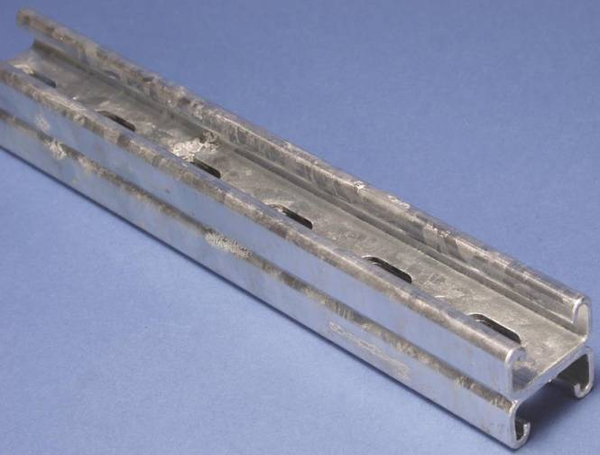 Eine Nahaufnahme einer Metallschiene vor blauem Hintergrund, die Rillen und eine leicht abgenutzte Oberflächentextur zeigt.