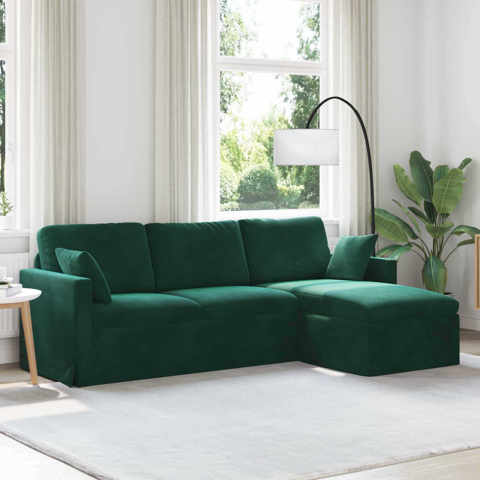 Ein grünes Sofa mit Chaiselongue steht in einem hellen Wohnzimmer, akzentuiert durch eine Stehlampe und eine Topfpflanze. Große Fenster lassen natürliches Licht herein.