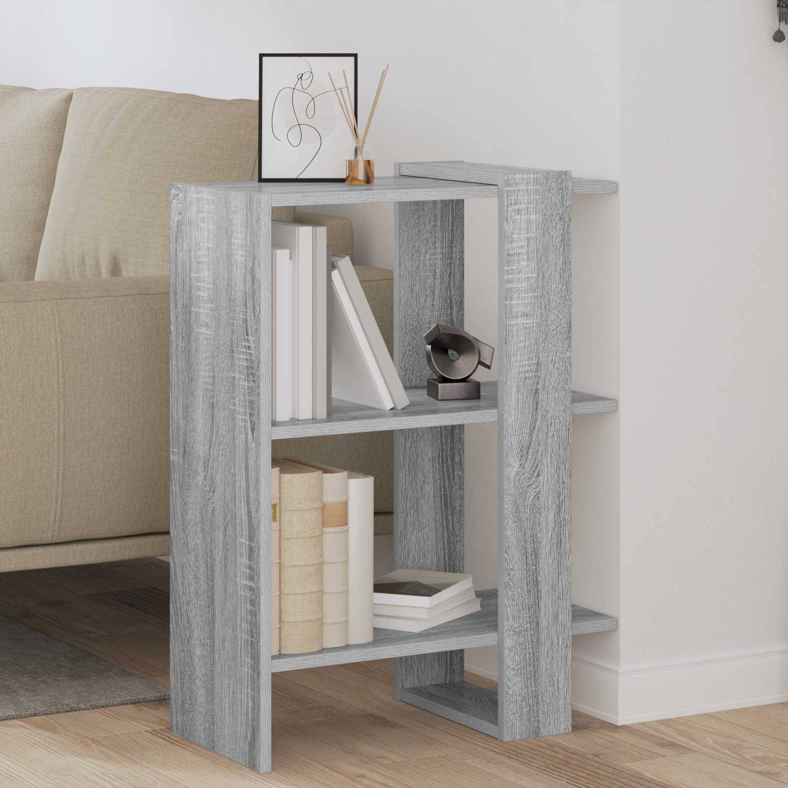 Grauer Holzmaserung-Nachttisch neben einem beigen Sofa, bestückt mit Büchern und kleinen Dekorationselementen in einem minimalistischen Wohnzimmer.