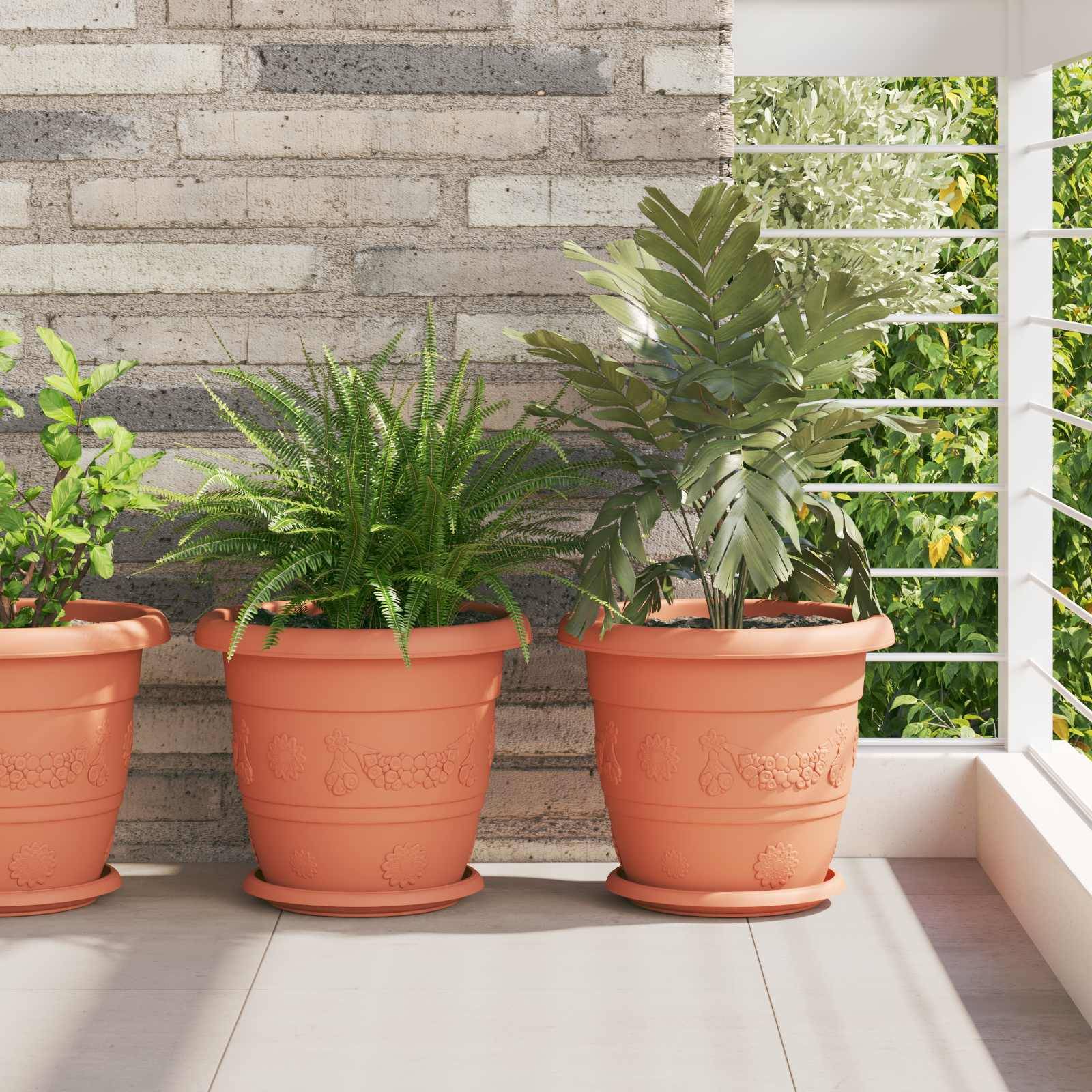 Drei Terrakottatöpfe auf einem sonnigen Balkon enthalten verschiedene grüne Pflanzen vor einer Backsteinmauer; eine moderne, helle und natürliche Umgebung.