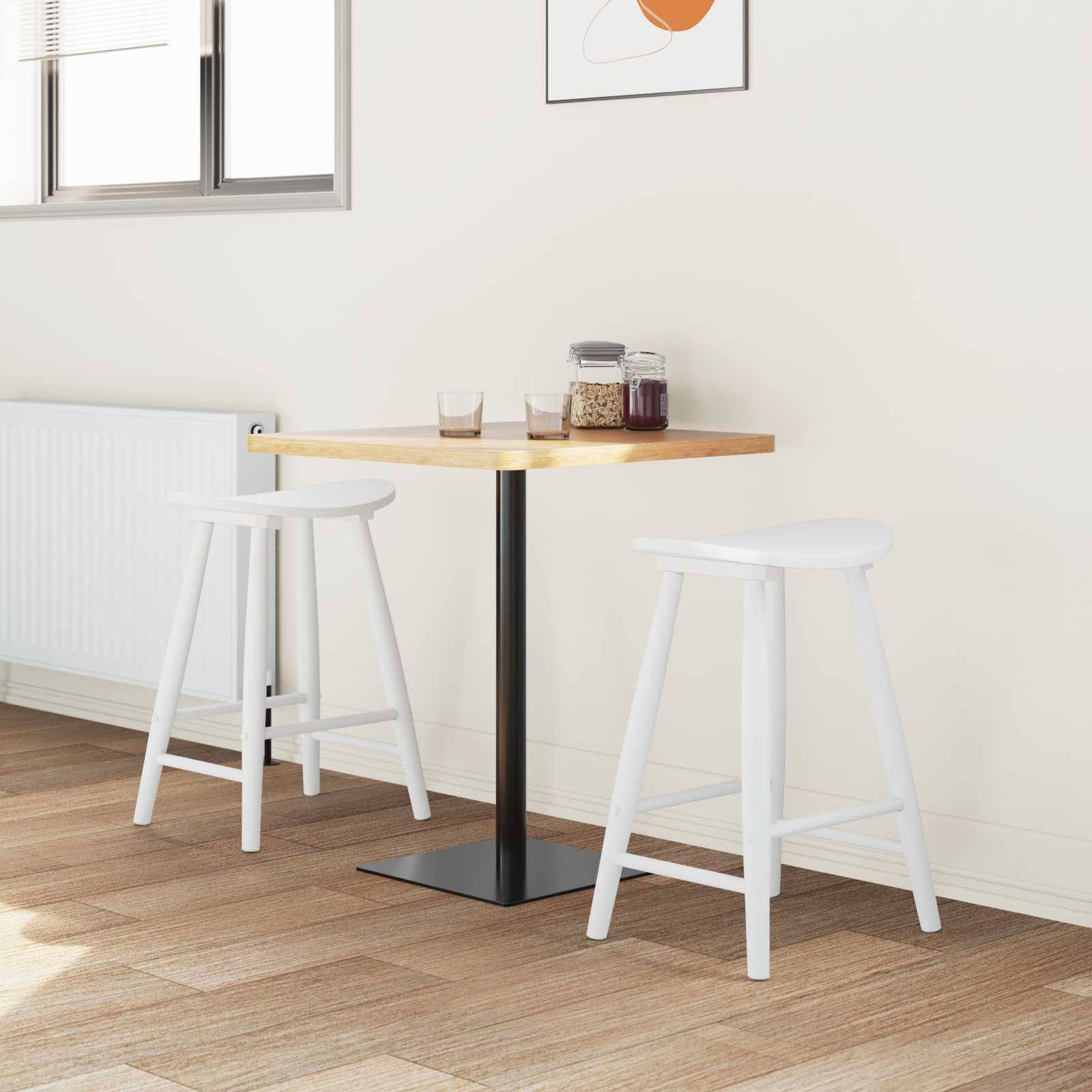Eine moderne, minimalistische Kückenecke mit einem kleinen quadratischen Holztisch, zwei weißen Hockern und einem Fenster. Ein gerahmtes abstraktes Kunstwerk hängt an der Wand.