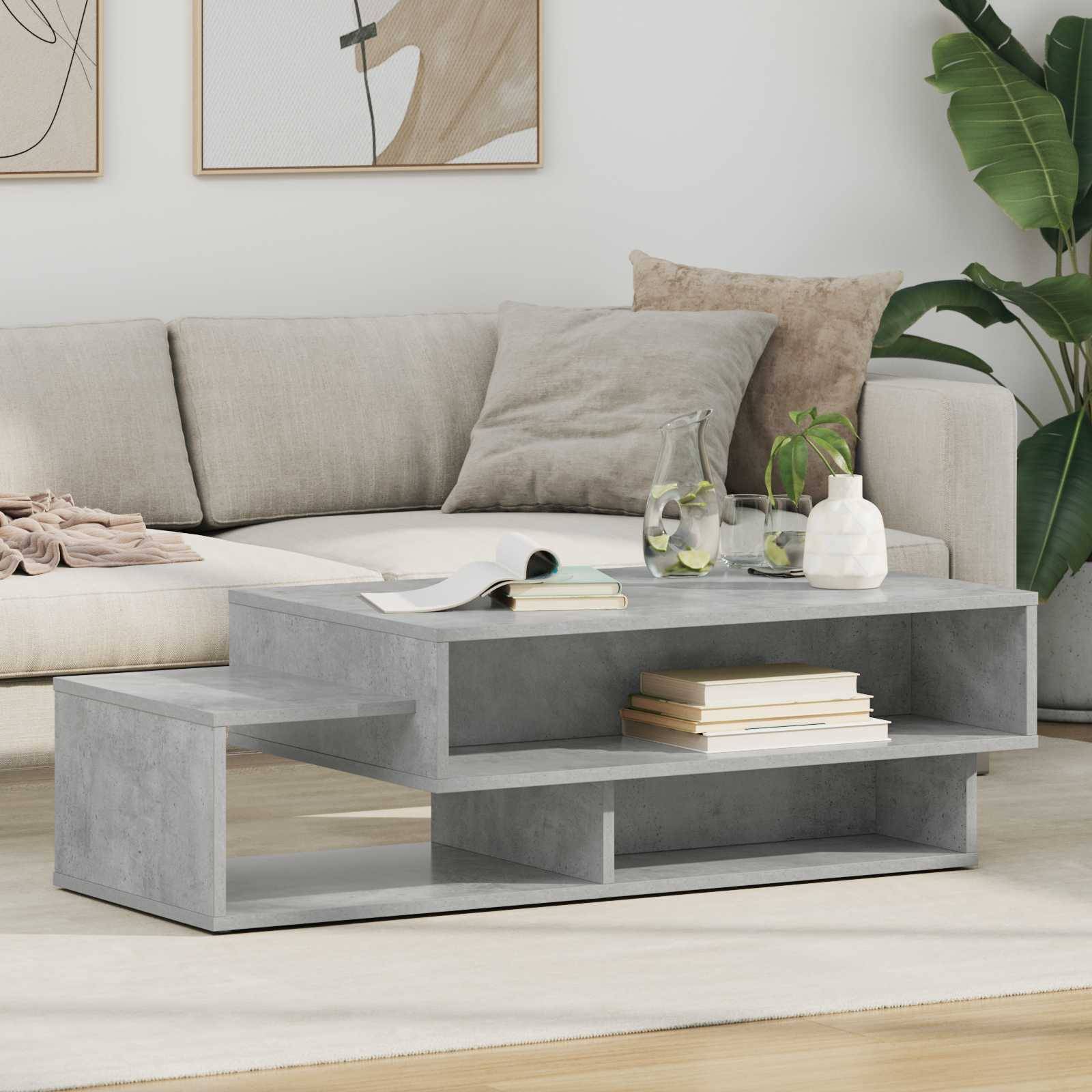 Ein modernes Wohnzimmer mit einem hellgrauen Sofa mit beigen und braunen Kissen, einem grauen geometrischen Couchtisch mit einer Pflanze und Büchern.