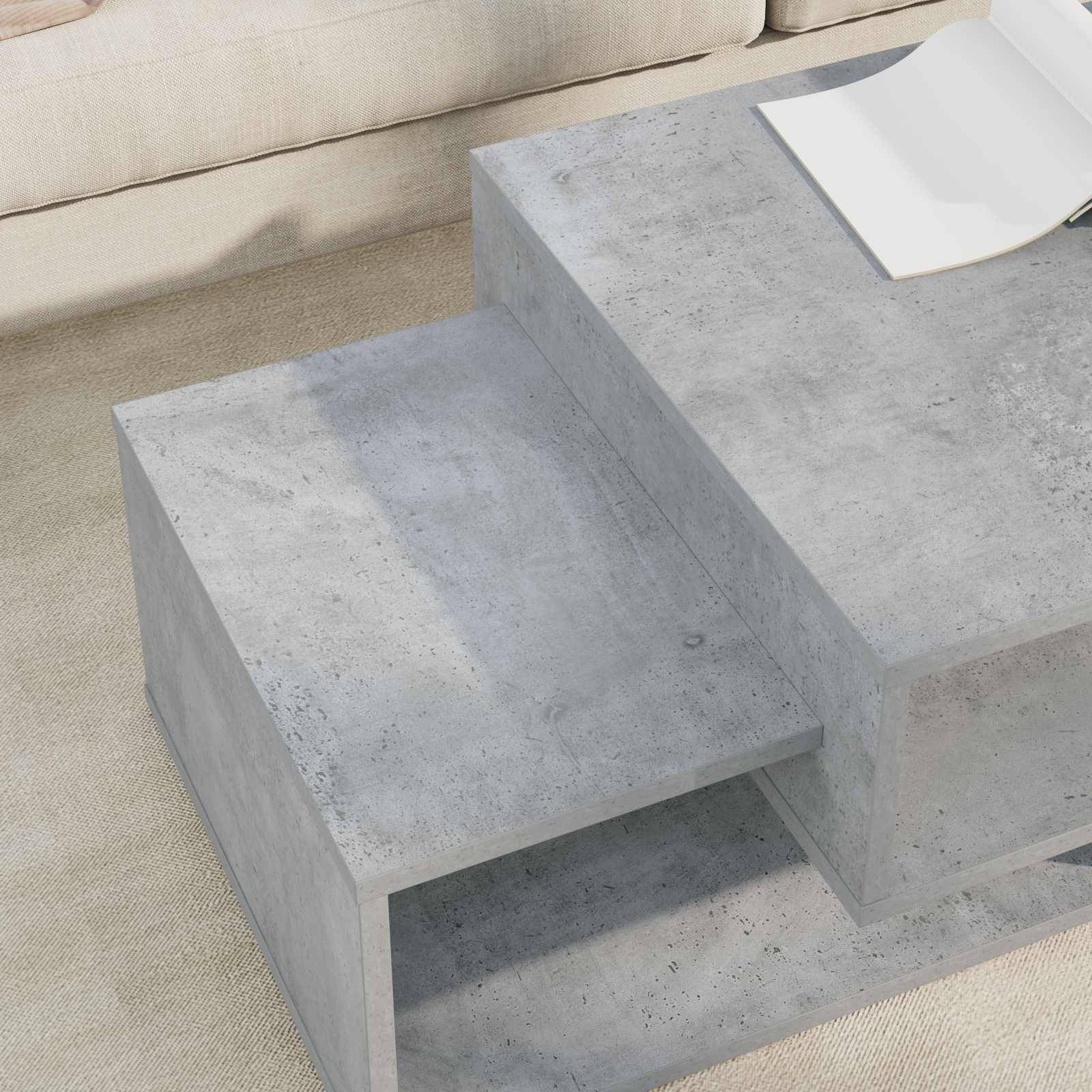 Betonnen Couchtisch mit gestaffelten Ebenen, auf dem ein aufgeschlagenes Buch liegt, platziert in einem Wohnzimmerinterieur mit einem beigefarbenen Sofa dahinter.