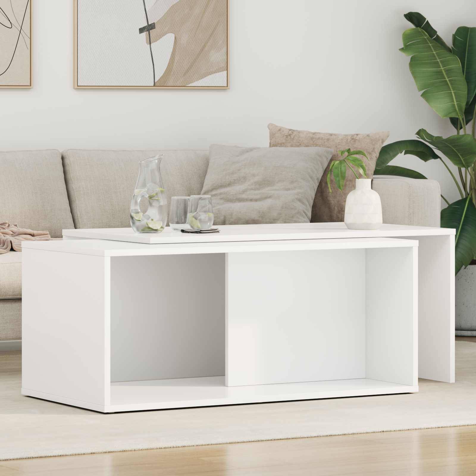 Modernes Wohnzimmer mit einem beigen Sofa, weißem Couchtisch mit Gläsern und einer Pflanze obenauf, und einer großen grünen Pflanze in der Ecke.