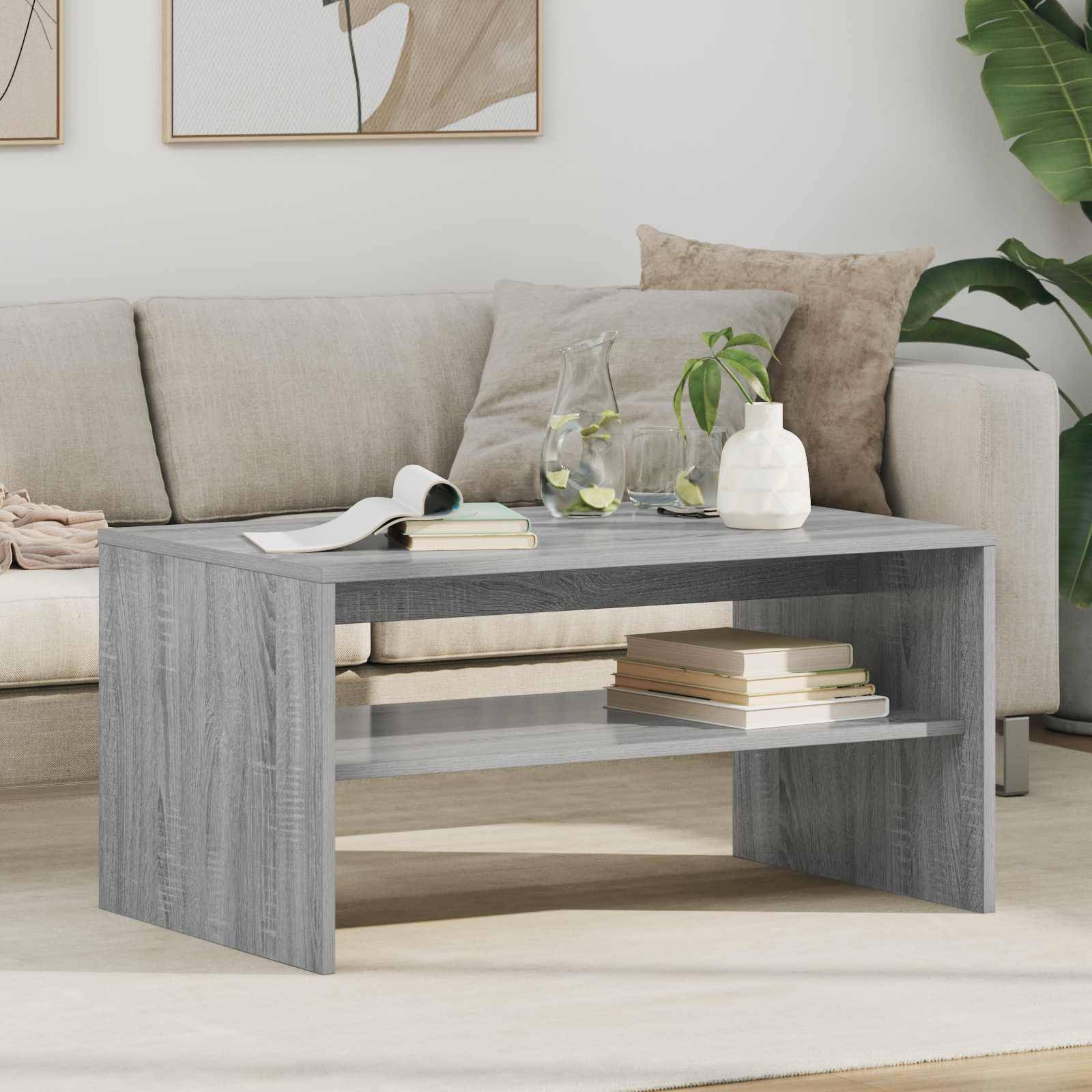 Ein modernes Wohnzimmer mit einem hellgrauen Sofa, das mit Kissen verziert ist. Ein grauer Holzcouchtisch hält Bücher und ein Glas Wasser.