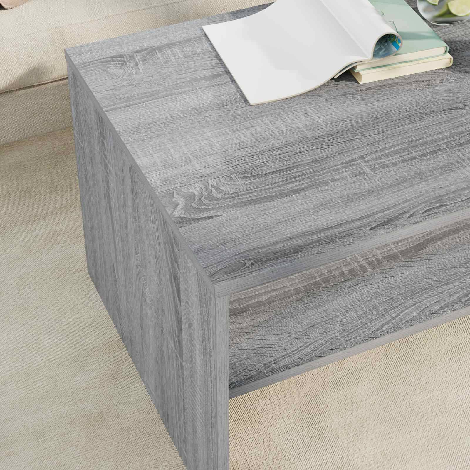 Ein grauer Holz-Couchtisch mit glatter Oberfläche. Ein aufgeschlagenes Buch ruht darauf, während ein weiteres Buch teilweise darunter sichtbar ist.