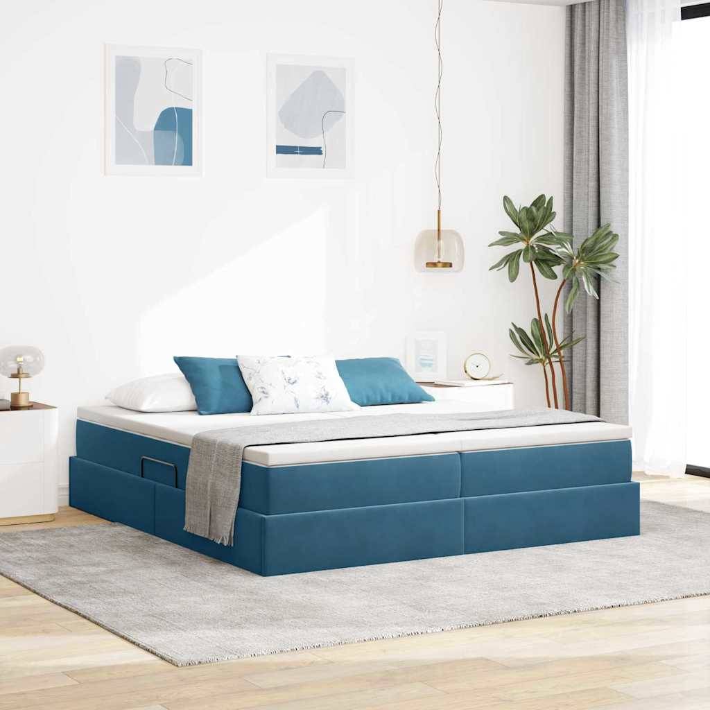 Blaues Bett mit weißen Laken und Kissen in einem hellen Zimmer. Es gibt zwei hängende Leuchten, eine Pflanze und minimalistische Kunst an den Wänden.