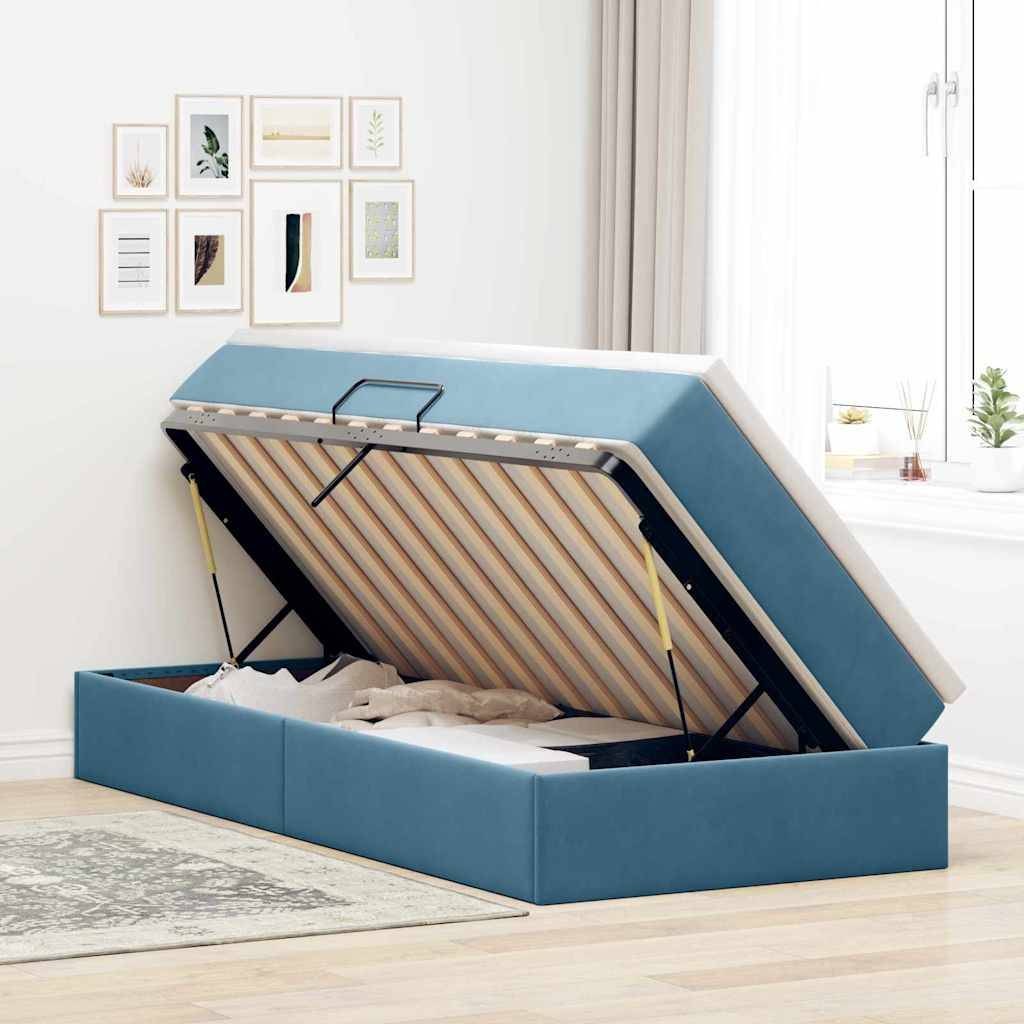 Ein blau gepolstertes Bett mit hydraulischem Lift zeigt Stauraum darunter. Das Zimmer hat Wandkunst in Rahmen und ein Fenster mit Sonnenlicht.