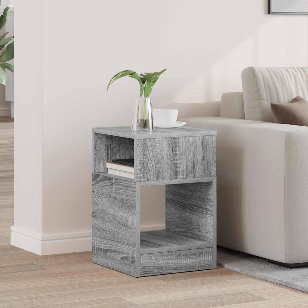 Ein kleiner grauer Holzbeistelltisch mit einer Vase, die grüne Blätter enthält, neben einem beige Sofa in einem hell erleuchteten Wohnzimmer platziert.