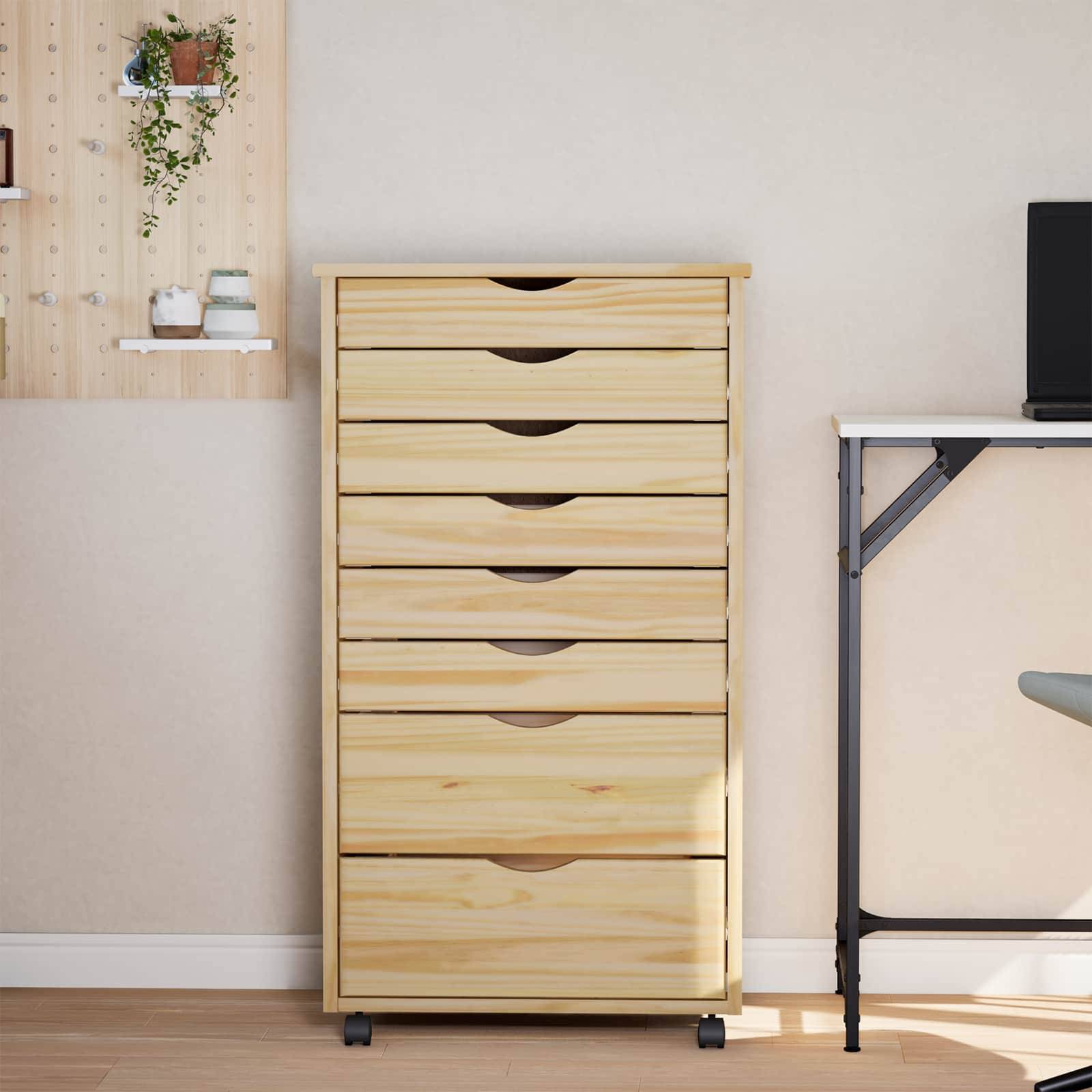 Eine Holzkommode mit sechs Schubladen steht neben einem weißen Wandregal mit Pflanzen und Dekorationselementen, neben einem modernen Schreibtisch.