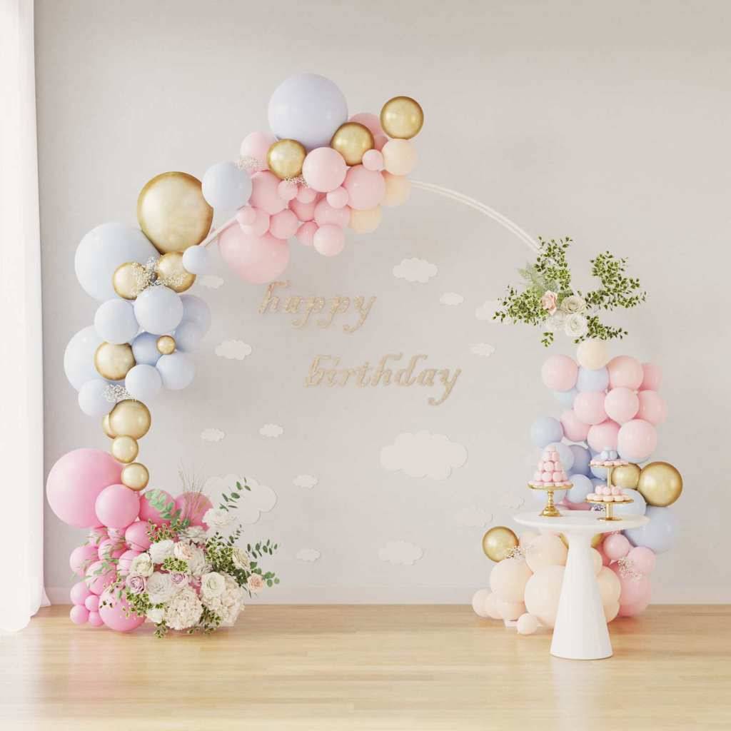 Ein Ballonbogen in Pastellfarben mit goldenem Akzenten und Blumenarrangements rahmt einen kleinen Tisch mit Süßspeisen unter einem „Alles Gute zum Geburtstag