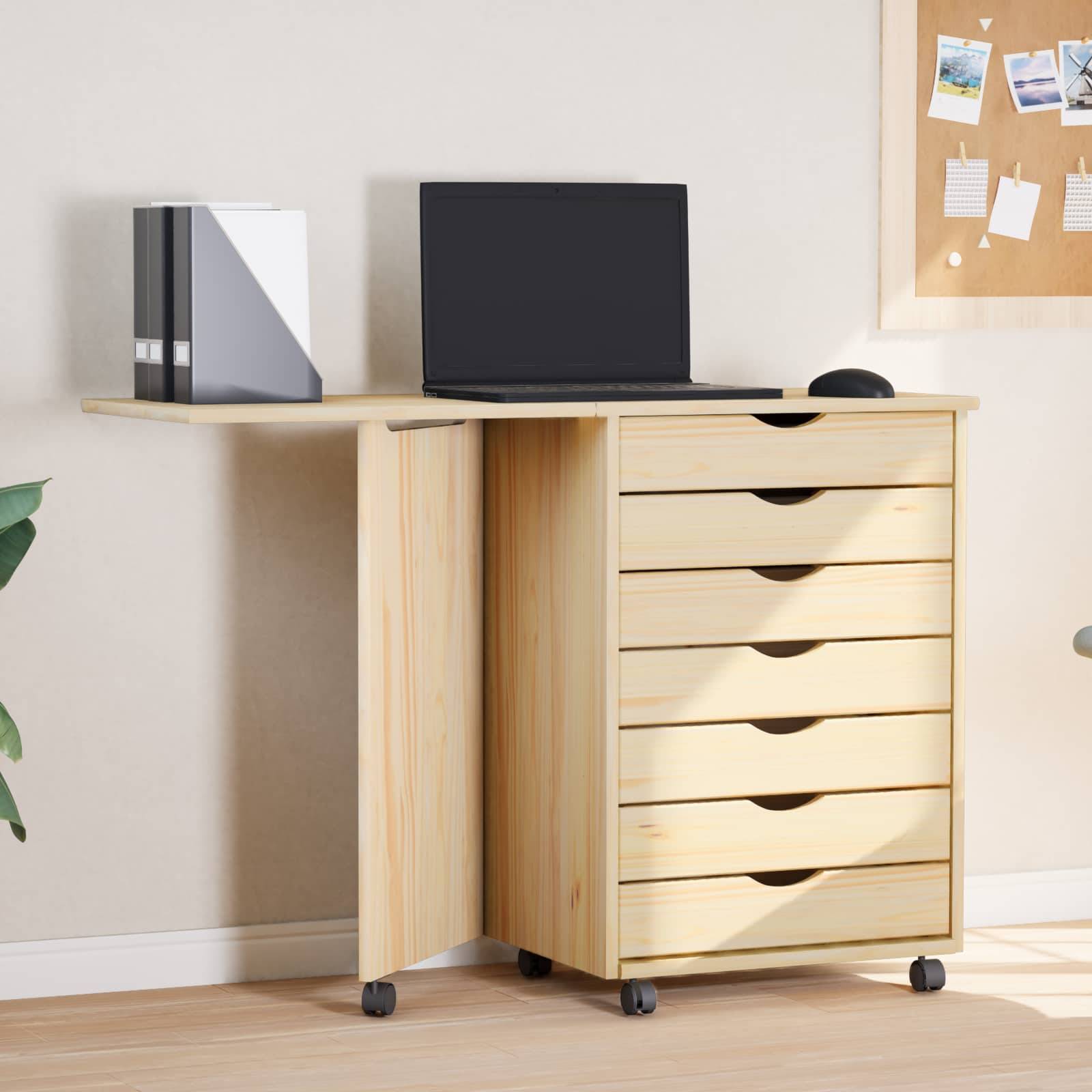Ein heller Holzschreibtisch mit Schubladen zur Aufbewahrung, auf dem ein Laptop, zwei Bücher und eine Topfpflanze stehen, neben einer Wand mit hängenden Bildern.