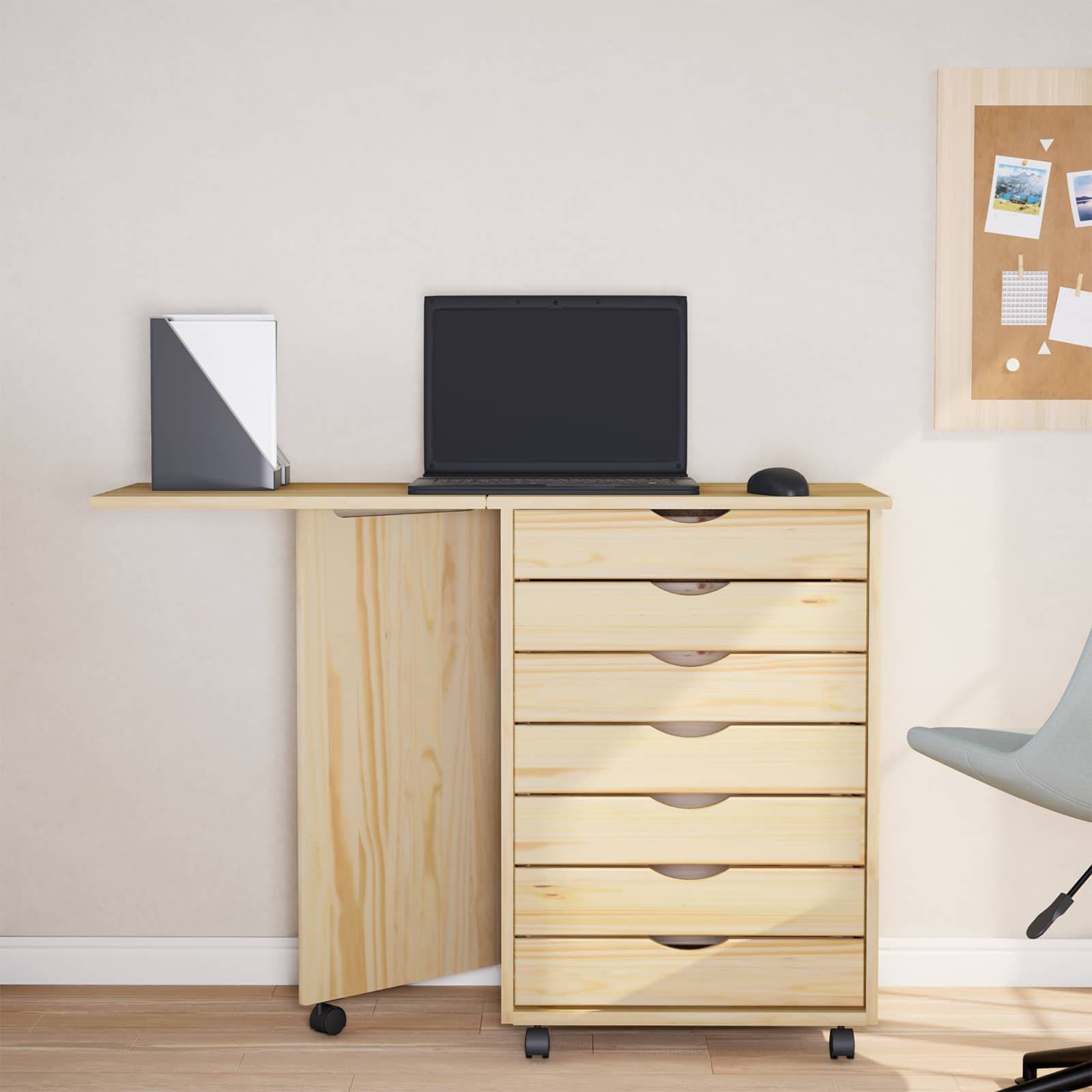Ein minimalistisches Home-Office-Setup mit einem Holzschreibtisch, einem geschlossenen Laptop, einem kleinen Lautsprecher und einer Pinnwand mit angesteckten Notizen und Fotos an der Wand.